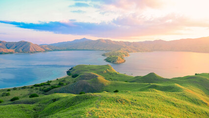 Panoramic background of mountains, sea, trees, sunset light in the sky, green hills and blue ocean at Gili Lawa, Komodo National Park, Indonesia. summer background and summer holiday concept.  © Balnyes Visuals