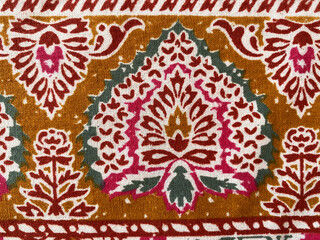Intricate peacock-inspired floral motifs in mustard, green, pink, and maroon are hand block printed...