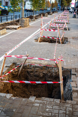 Repair of Square Holes on Sidewalk with Red and White Safety Tape Barricades. Road Repair Area....