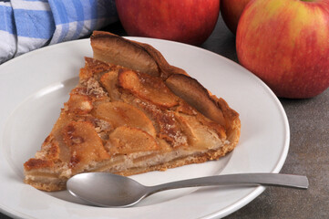 Part de tarte aux pommes maison servie dans une assiette avec une cuillère avec des pommes à côté