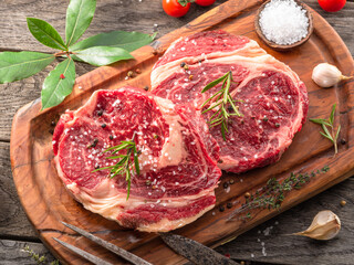 Raw beef steaks with herbs and spices ready for cooking are on wooden board.