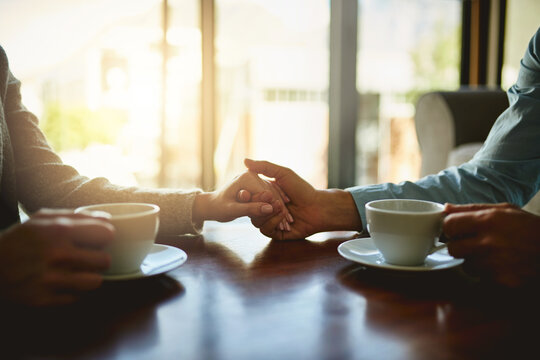 People, holding hands and coffee in home with love, support and trust in relationship. Tea time, couple and gesture in living room for compassion, hope and healing for emotional wellness with care