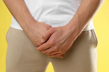 STD (sexually transmitted diseases). Man suffering from symptoms on yellow background, closeup