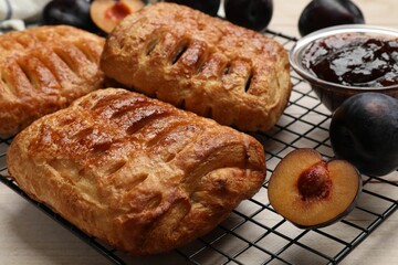 Delicious puff pastries and plums on white wooden table, closeup