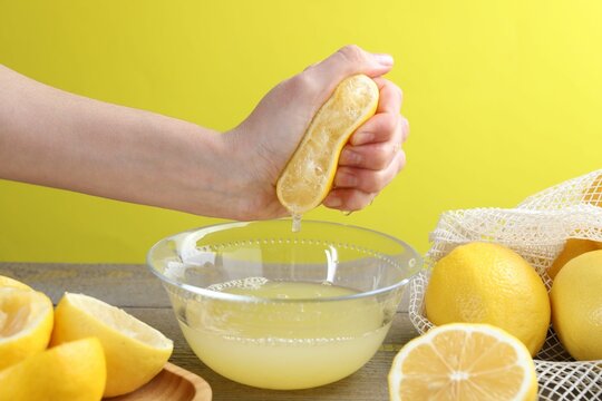 Woman squeezing lemon juice into bowl at wooden table, closeup - Powered by Adobe