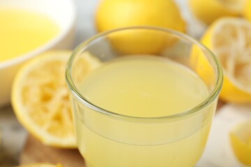 Glass of fresh lemon juice and squeezed fruits on table, closeup