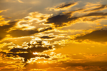 Obraz premium the evening sky illuminated by the sun hidden behind a cloud. evening sky with clouds and sun. the sun hides behind the clouds during sunset