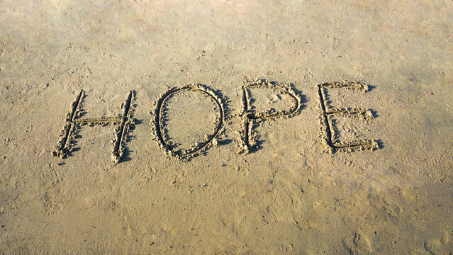 The word "HOPE" written in the sand on a sunny beach, symbolizing optimism and positivity.