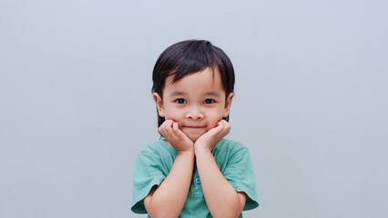 Studio portrait of a adorable little boy holding his cheeks with his hands on a grey background © arthierry