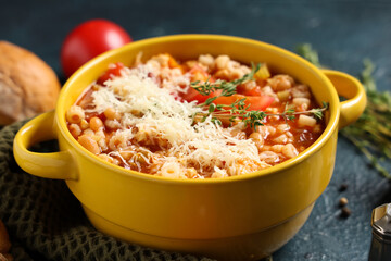 Bowl of pasta fagioli with cheese and thyme on dark background