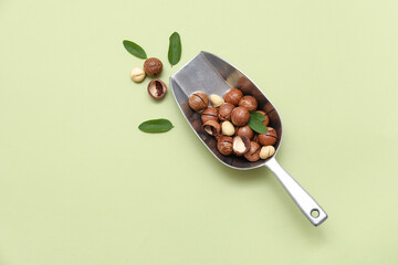 Metal scoop with tasty macadamia nuts and leaves on green background