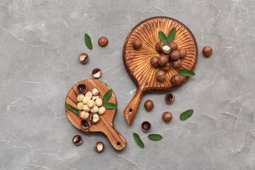 Wooden boards with tasty macadamia nuts and leaves on grey background