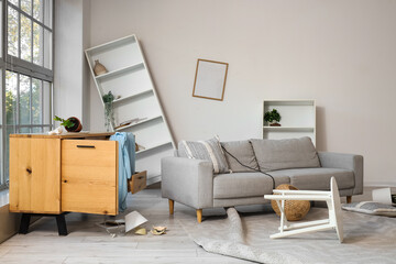 Interior of messy living room with sofa, drawers and shelf units after earthquake