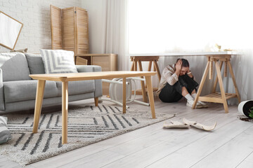 Young woman hiding under table in messy living room during earthquake