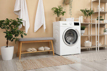 Interior of stylish bathroom with shelving units, washing machine and grey bench