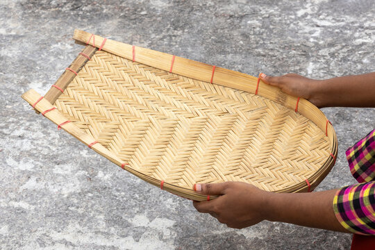 A female hand holds an empty Kula, also known as Kulo. Made from bamboo cane, It is a traditional tool essential for Bangladeshi farmers to separate grain from chaff by tossing it in the air.