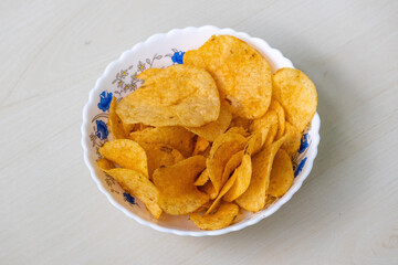 A bowl of crispy potato chips on light wooden Surface. Delicious spicy lays potato chips.