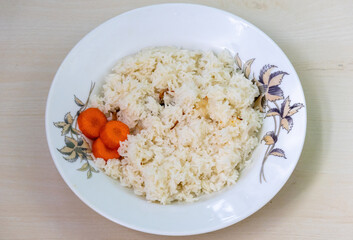 Homemade aromatic rice dish Polao or Pulao, with carrots in a white plate, placed on a wooden background. It is very tasty food often served with mutton or beef curry in Bangladesh and India.