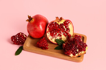 Wooden board with fresh ripe pomegranates and leaves on pink background