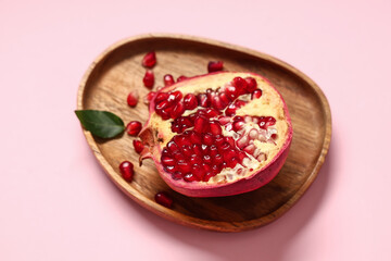Wooden tray with half of fresh ripe pomegranate and seeds on pink background