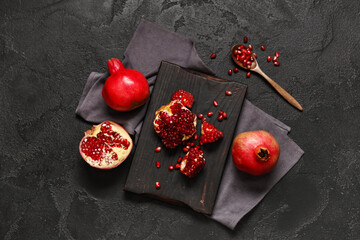 Wooden board with cut fresh pomegranate and spoon of seeds on black background