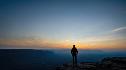 Fototapeta premium Silhouetted figure gazing over a vast canyon during sunset, capturing the serene beauty of nature's twilight colors