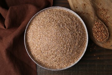 Buckwheat bran in bowl and grains on wooden table, top view
