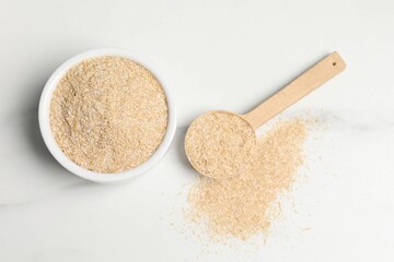 Oat bran in bowl and spoon on white marble table, top view