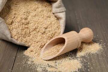 Oat bran in burlap bag and scoop on wooden table, closeup