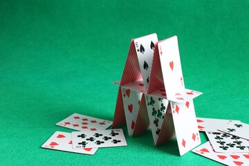 Collapsed house of playing cards on green background. Space for text