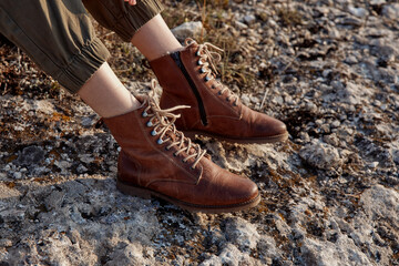 Naklejka premium Woman's legs in brown boots on rocky surface with rocks in the background for travel and adventure concept