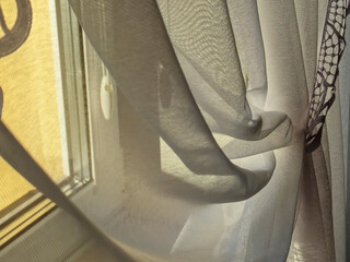 Soft curtains draped by a window, allowing warm sunlight to filter through, creating a serene...