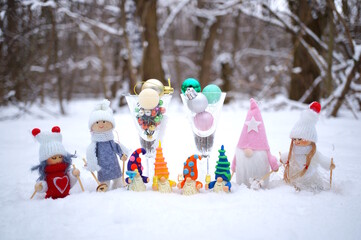 Fabulous toy characters in the winter forest. Four dwarfs with glasses of champagne and Christmas angels. Next to it are two glasses with Christmas balls.