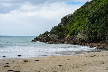 Fototapeta premium Scenic Coastal View of a Serene Beach with Rocky Outcrops and Lush Greenery Under Overcast Skies, Perfect for Relaxation and Nature Photography