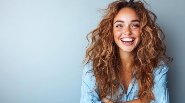 A captivating woman with flowing hair and a dazzling smile radiates youthful excitement and warmth, highlighted by a minimalistic and calming blue background.