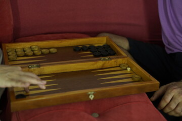 Close-up of people playing backgammon at home, focusing on the hands moving the pieces and rolling the dice.