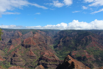 Waimea canyon - cloudy and clear skies, landscape view, long horizon, red lava rocks, green foliage. 