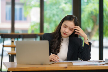 Beautiful Asian businesswoman using a laptop working in an office and depressed.