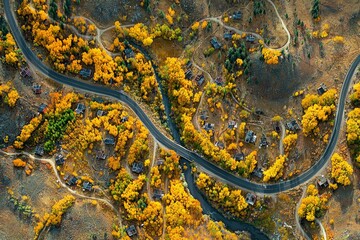 Aerial view of a winding road through an autumn-hued aspen forest in the mountains of Colorado, with small villages