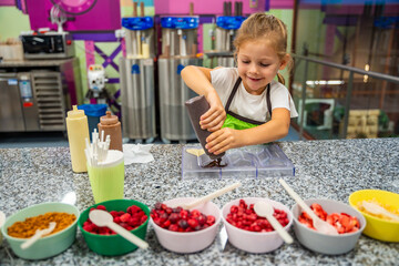 Little girl learning how to cook in a cooking class. Handmade dessert. Making chocolate candy, Child filling heart shaped mold with chocolate