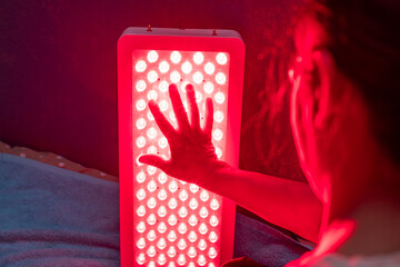 Senior Woman touching Red Light Therapy Panel LEDs with hand at home