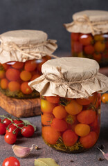 Pickled cherry tomatoes with garlic in glass jars on brown table