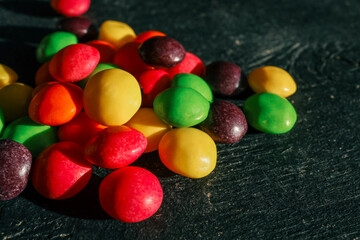 Close-up of colorful candy-coated chocolates in vibrant red, yellow, green, orange, and purple tones, arranged in a textured pattern. Bright, sweet, and vivid confectionery backdrop