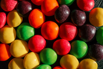 Close-up of colorful candy-coated chocolates in vibrant red, yellow, green, orange, and purple tones, arranged in a textured pattern. Bright, sweet, and vivid confectionery backdrop