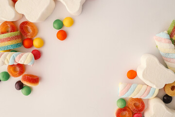 A cheerful flat lay composition of assorted colorful candies and marshmallows arranged on a light...