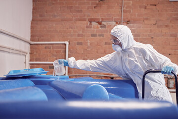Side view of female production operator wearing protective glasses and coverall pouring in open...
