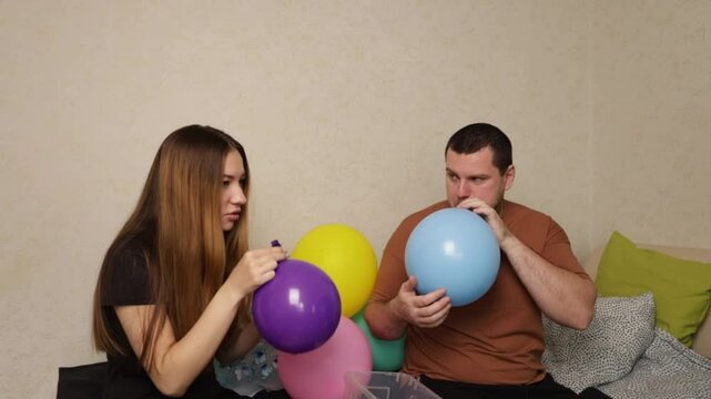 Father and daughter Blowing Up Balloons for Party Decoration, man and child inflating colorful balloons at home, fun family activity of decorating for a party.