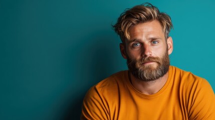 Obraz premium This image features a man with a beard wearing a vibrant orange shirt contrasted against a teal textured wall, showcasing colorful style and expressive character.