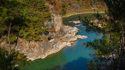 Autumn scenery of the Hantan River Columnar Joint Road, with canyons and cliffs formed by the river flowing through the volcanic terrain. (emerald water, blue sky and colorful leaves)