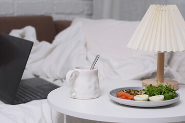 Enjoying a Cozy Breakfast in Bed with a Laptop and Warm Lamp for Comfort and Relaxation